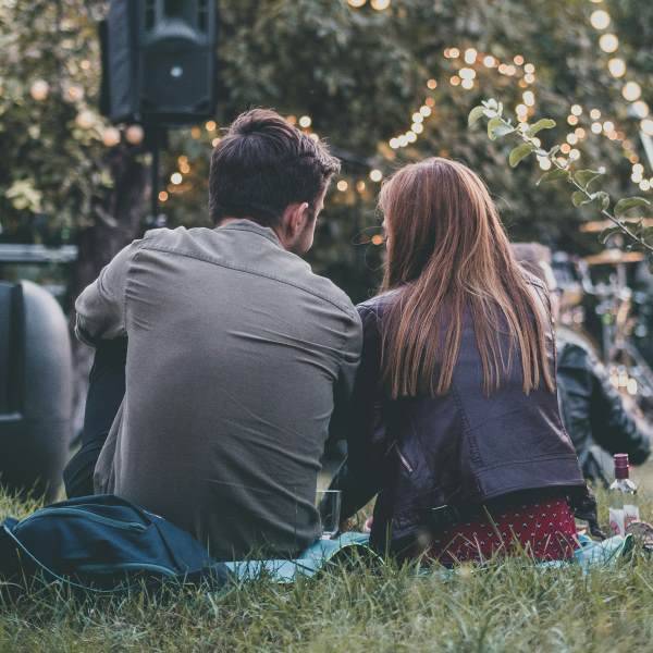 Quelle: Bild von Alexandra Marta auf unsplash Ein Mann und eine Frau sitzen auf einer Wiese mit Blick auf eine beleuchtete Außenkulisse